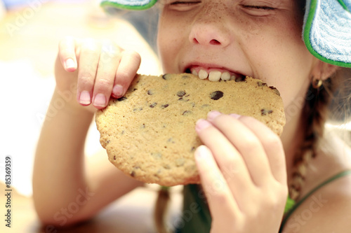 Young girl eating a big cookie outside in the summer.