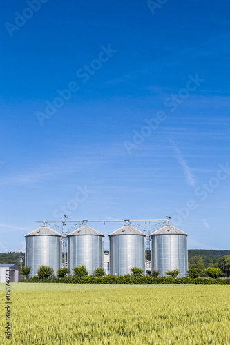four silver silos in field under bright sky