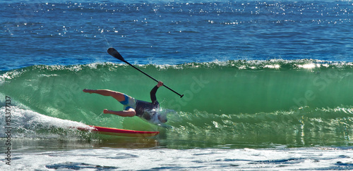 Konstfotografi A paddleboarder loses his balance as he rides a big wave in to shore
