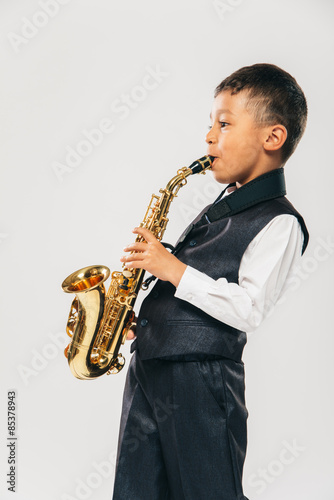 six years old boy plays saxophone at studio