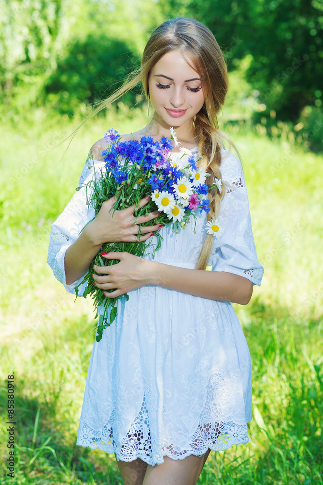 Young charming woman holding flower bouquet with camomiles and cornflowers and smiling, against green summer nature Young charming woman holding flower bouquet with camomiles and cornflowers and smiling, against green summer nature
