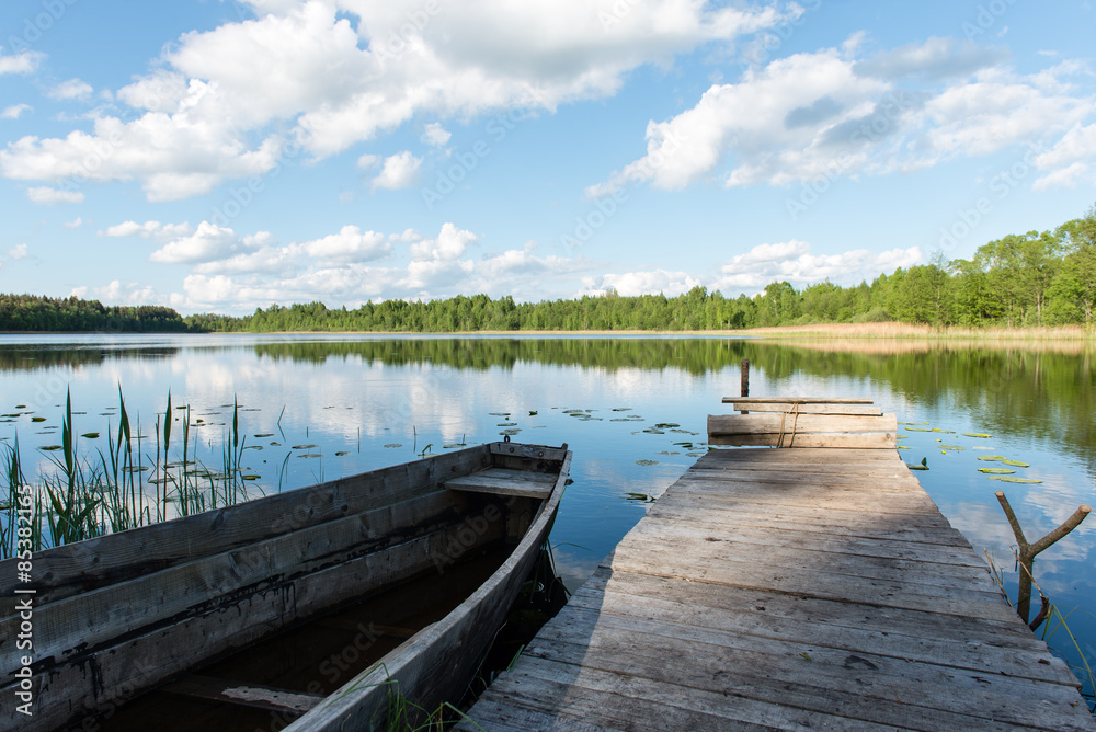 Naklejka premium Białe chmury na niebieskim niebie nad niebieskim jeziorem z łodziami i deską