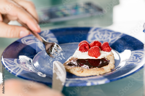 Eating pancakes dessert with raspberry, cream and chocolate crea