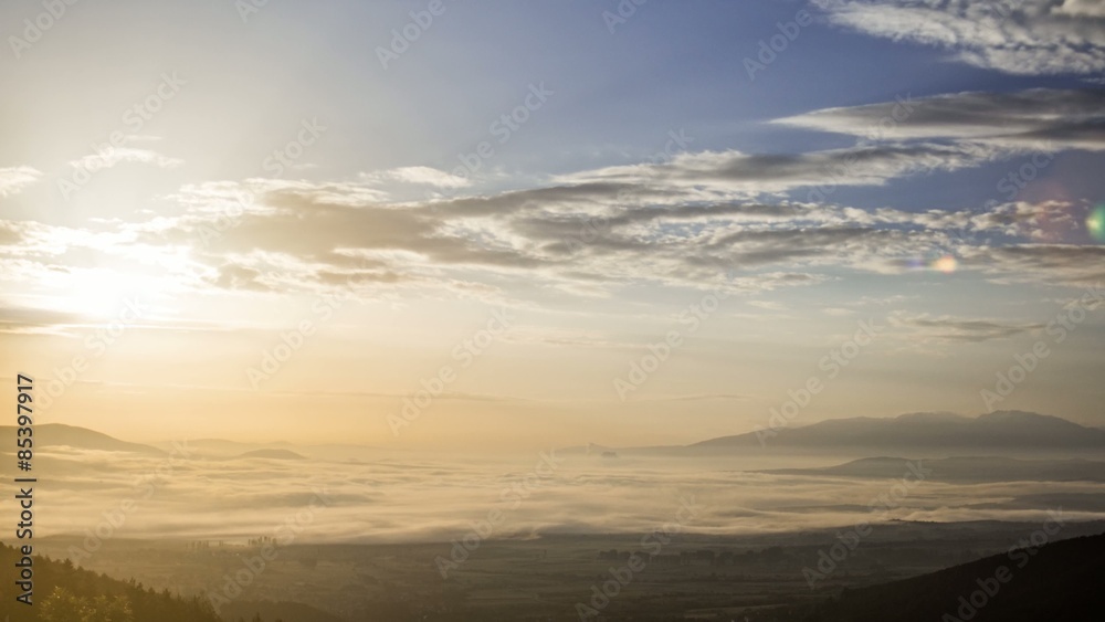 Foggy Field and Clouds Sunrise; A big field with a thin layer of fog above it, moving very smoothly. The sun is rising & there is a natural lens flare Foggy Field and Clouds Sunrise; A big field with a thin layer of fog above it, moving very smoothly. The sun is rising & there is a natural lens flare