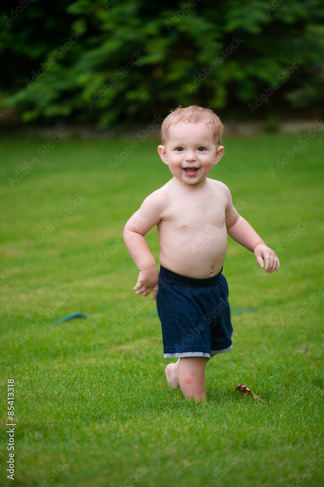 Toddler cools off by playing in water sprinkler at home in his b Toddler cools off by playing in water sprinkler at home in his b