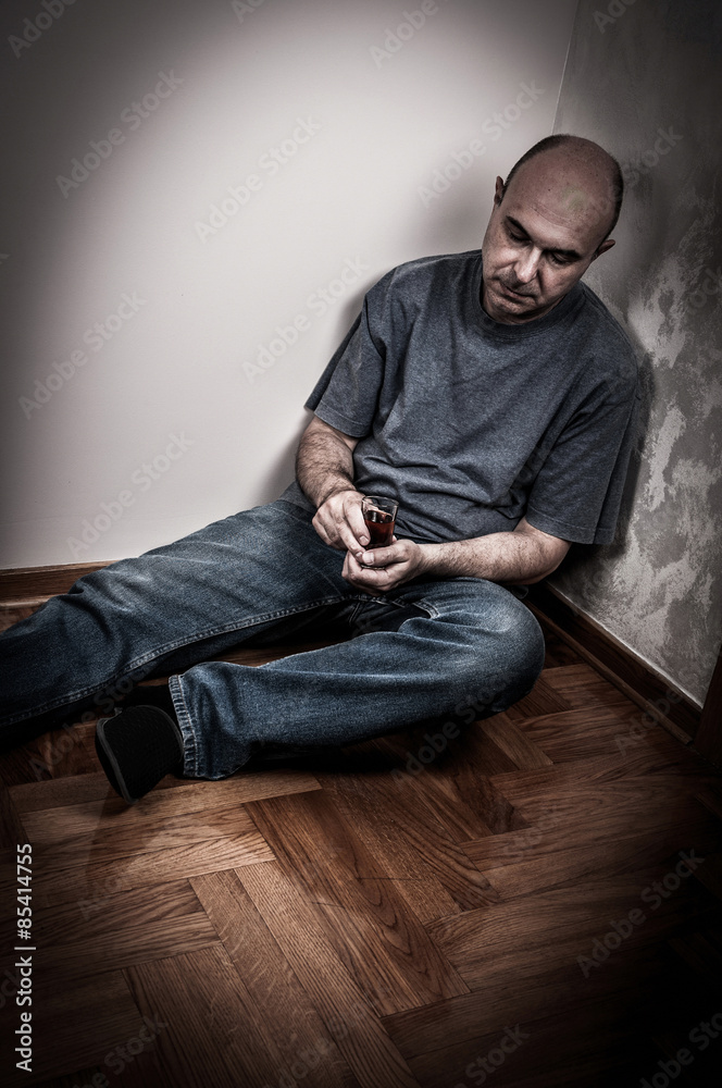 Drunk man sitting on the floor, sleeping and holding a glass of alcohol drink Drunk man sitting on the floor, sleeping and holding a glass of alcohol drink
