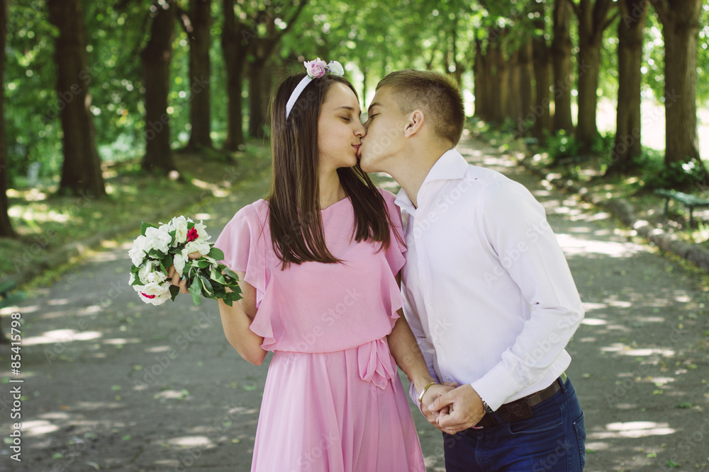 Fototapeta premium Newlyweds tseltsyutsya in the park. Bride is holding a bouquet of beautiful flowers