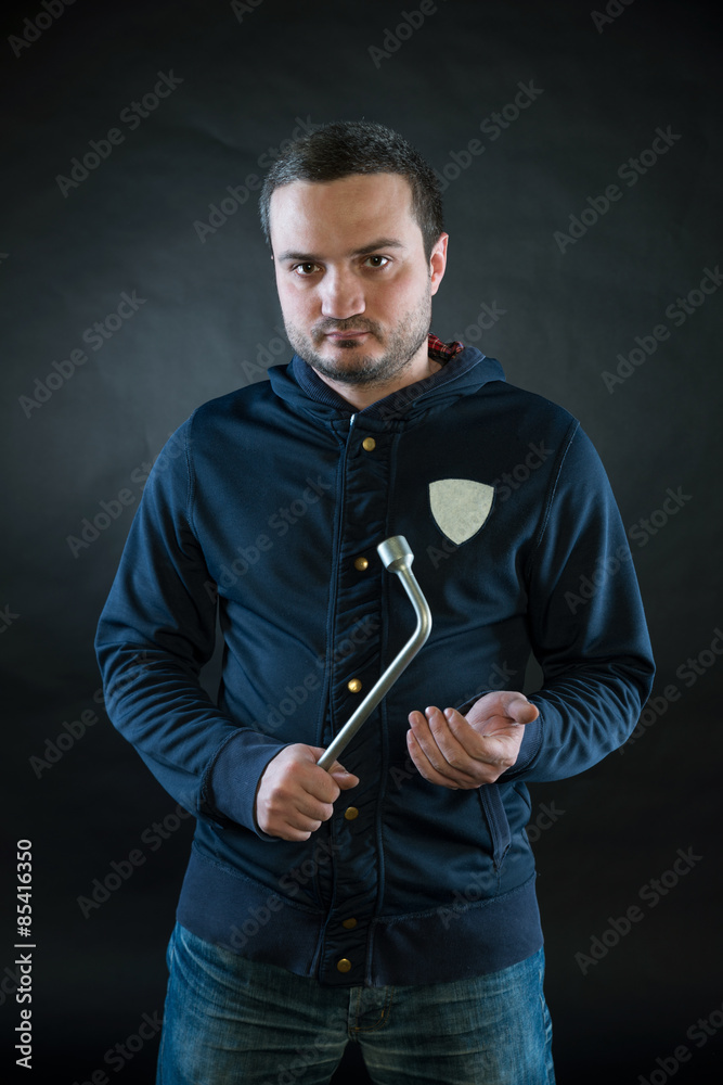 Mechanic with car wheel unscrewing key. Dark background. Mechanic with car wheel unscrewing key. Dark background.