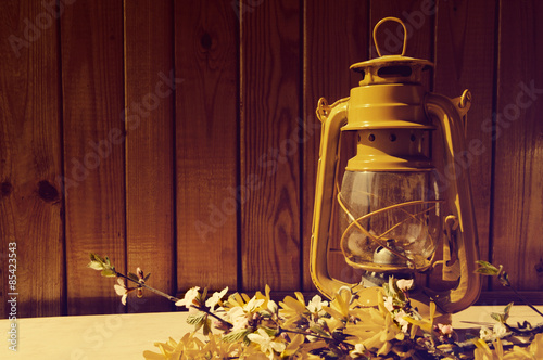 Yellow oil lamp and bouquet of spring yellow Forsythia colors against a wooden wall. A spring still life with an oil lamp. photo