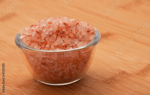 Himalayan pink salt in tiny transparent glass bowl on wooden bam