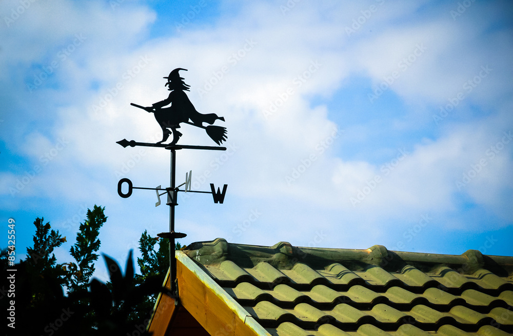 Black weathervane in the form of a witch.
The background has a blue sky with clouds. Black weathervane in the form of a witch.
The background has a blue sky with clouds.