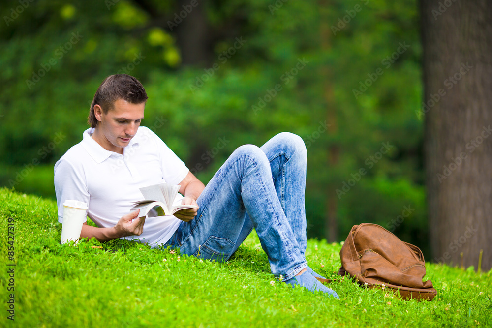 Young man relaxing with coffee in park reading a book Young man relaxing with coffee in park reading a book