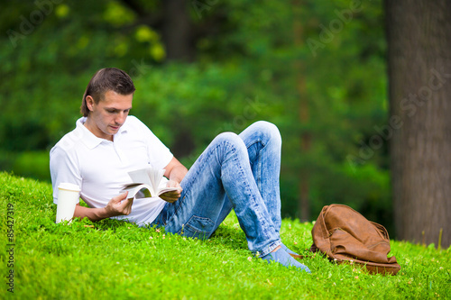 Young man relaxing with coffee in park reading a book
