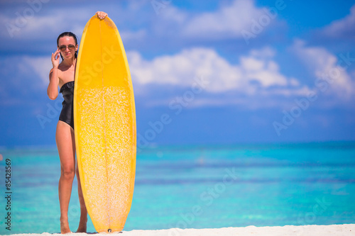 Happy slender surf woman at white beach with yellow surfboard