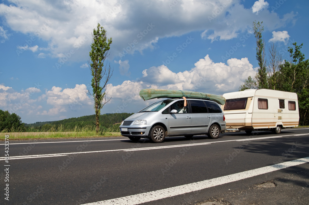 Car with a canoe on the roof and caravan traveling on the road. Traveling on vacation.