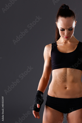 Muscular young woman standing on gray background