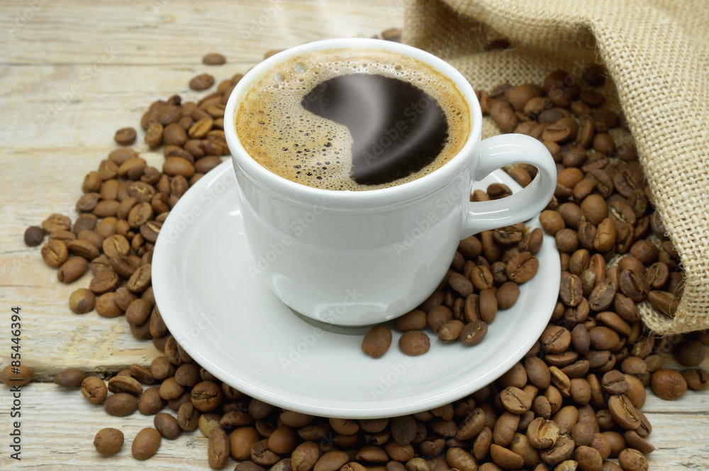 A Hot Cup of Strong and Flavored Coffee among Light Roasted Coffee Beans on a Wooden Table A Hot Cup of Strong and Flavored Coffee among Light Roasted Coffee Beans on a Wooden Table