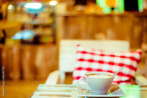 Cup of coffee on a wooden table with red pillow in cafe