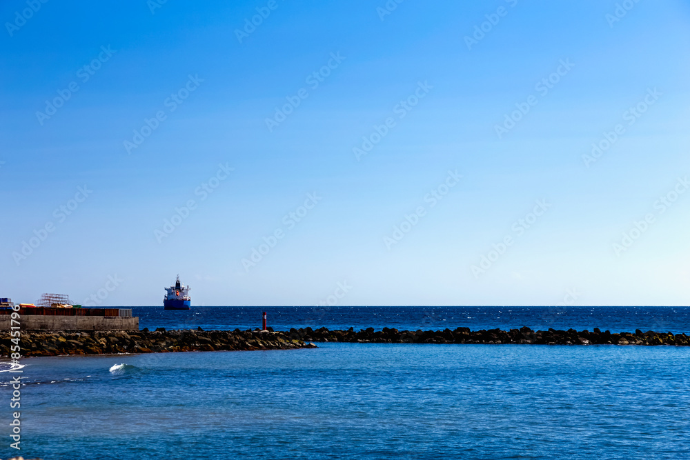 Cargo ship on the water in ocean. View from shore through breakwater