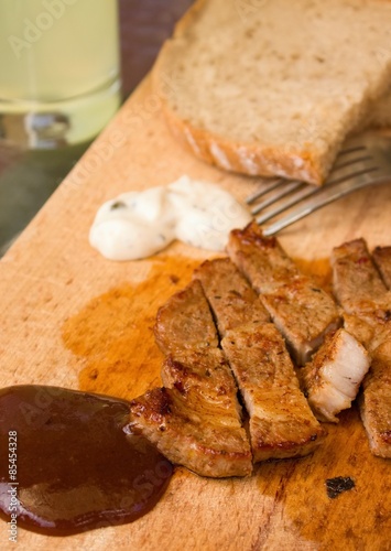 BBQ sauce with pork steak portion on wooden chopping board