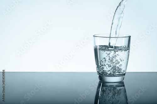 Glas auf Tischplatte wird mit Wasser gefüllt