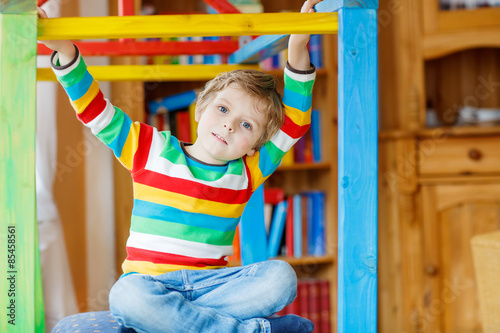 Little blond kid boy playing in selfmade wooden colorful house