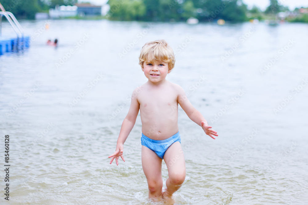 Little blond kid boy having fun with splashing in a lake, outdoo Little blond kid boy having fun with splashing in a lake, outdoo