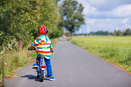 Kid boy in helmet riding his first bike, outdoors