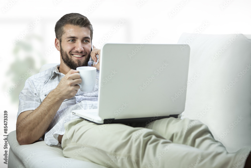 Attraktiver Mann liegt auf der Couch mit Notebook und telefoniert Attraktiver Mann liegt auf der Couch mit Notebook und telefoniert