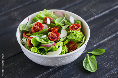 salad with fresh vegetables, garden herbs and sun-dried tomatoes in a white bowl 