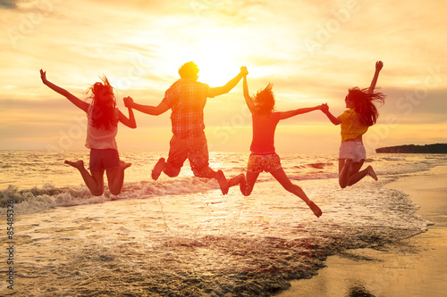 group of happy young people jumping on the beach
