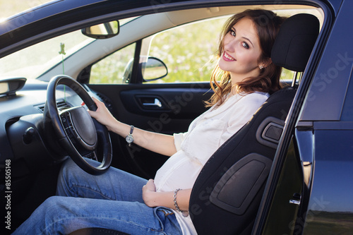 Pregnant happy young woman is sitting in black car