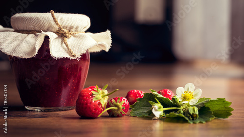 Homemade strawberry jam (marmelade) in jars on wooden background.