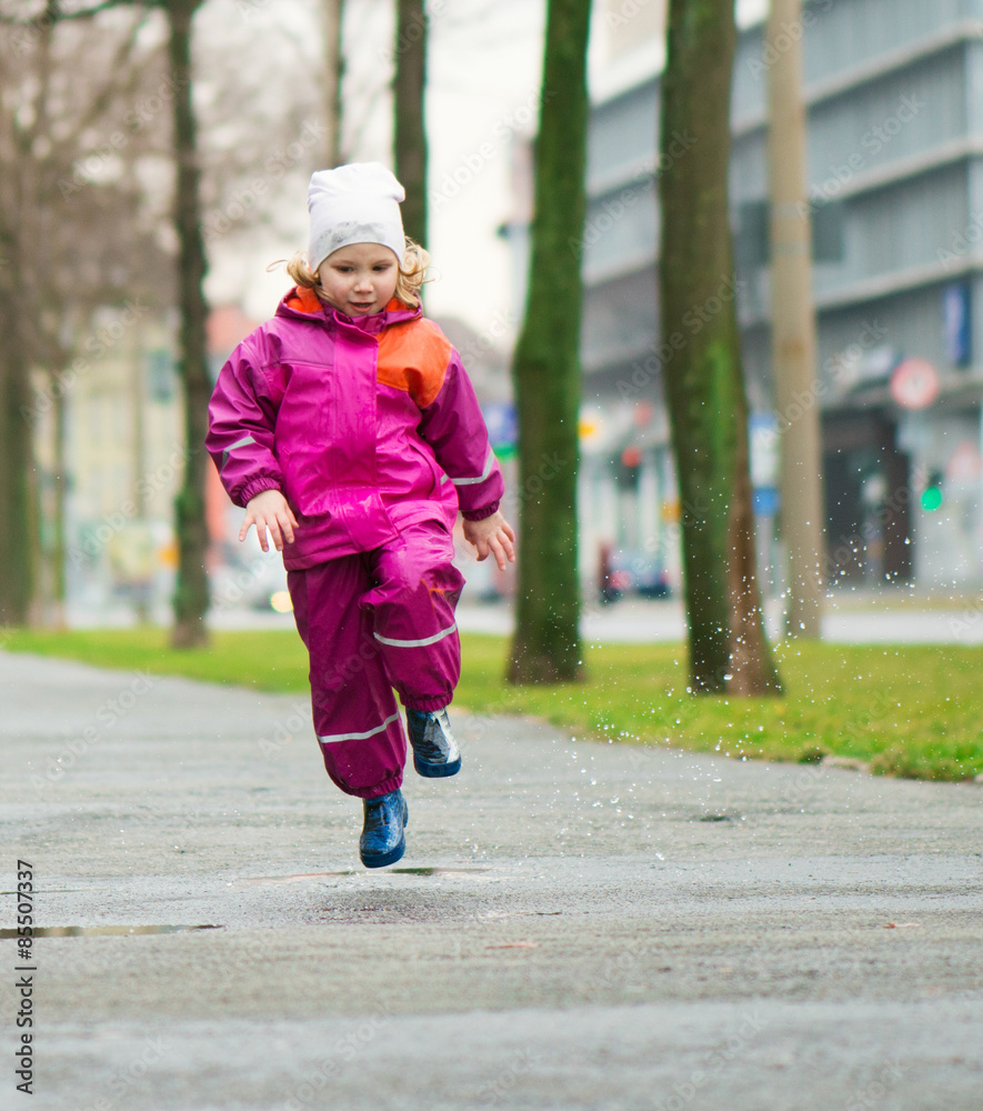 Fototapeta premium Little happy girl jumping in puddle