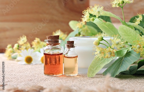 herbal cosmetic products bottles aroma oil, skincare cream, fresh flowers herbs leaves linden blossom