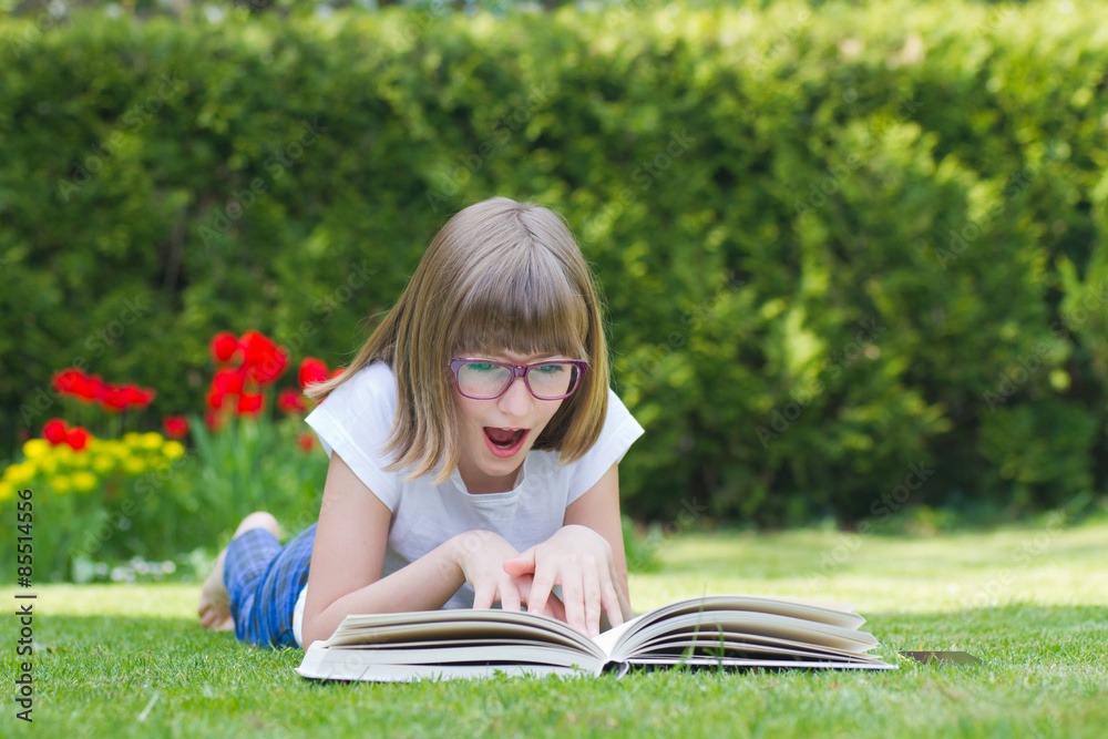 Girl astonished by reading a book in a garden Girl astonished by reading a book in a garden