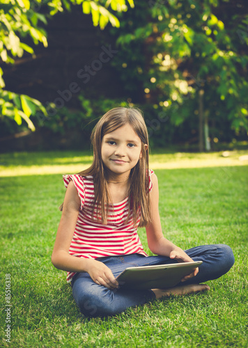 Toned photo of cute girl sitting on lawn and using digital table © Кирилл Рыжов