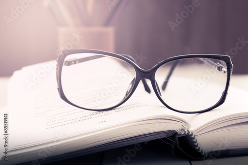 glasses on open book on wooden table in vintage color filter