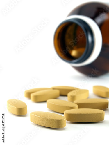close up group of oval medicine pills scattered out of opened glass drug bottle isolated on white background, health care with vitamins supplements to build immunity prevent sickness, vertical image