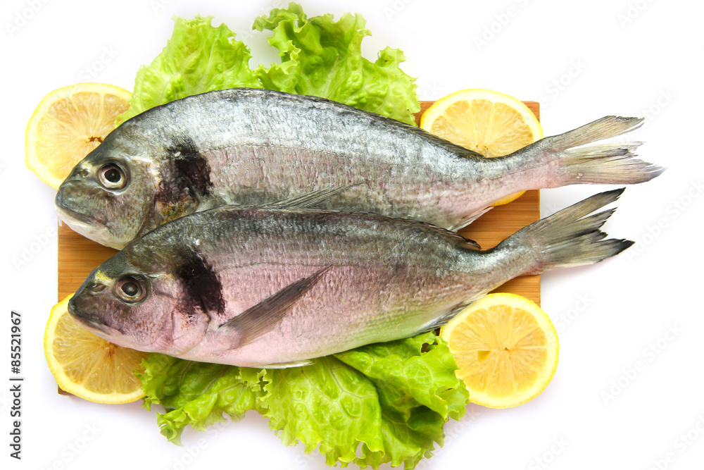 Fresh dorado on chopping board with lemon and vegetables Fresh dorado on chopping board with lemon and vegetables