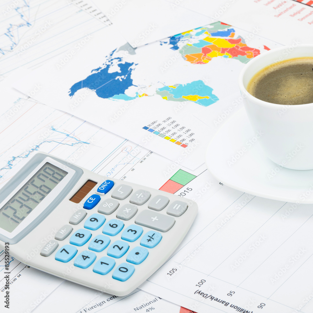Coffee cup and calculator over financial charts - close up shot Coffee cup and calculator over financial charts - close up shot
