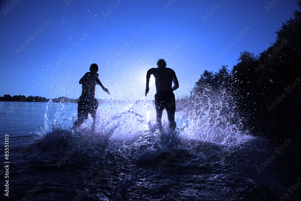 Glückliche junge Menschen laufen und springen am See beim Sonnenuntergang Glückliche junge Menschen laufen und springen am See beim Sonnenuntergang