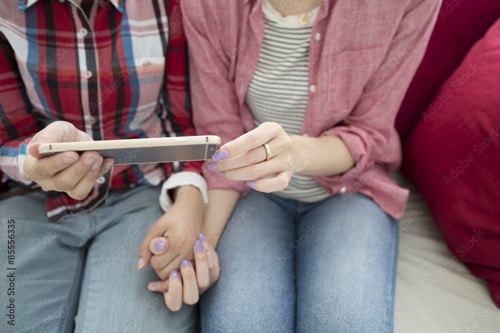 Two women looking at a smartphone hand in hand Two women looking at a smartphone hand in hand