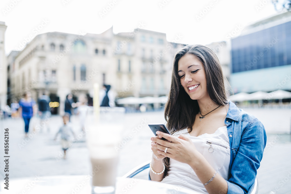Fototapeta premium Young smiling woman with a drink on a terraced while sending tex