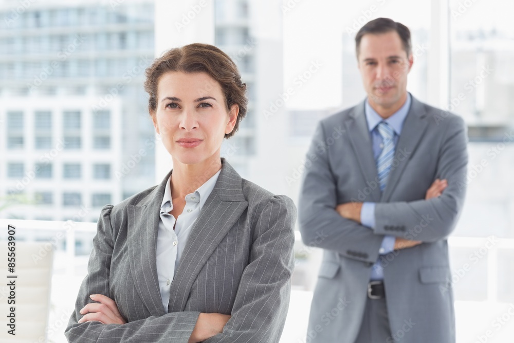 Businesswoman looking at camera with colleague in background Businesswoman looking at camera with colleague in background