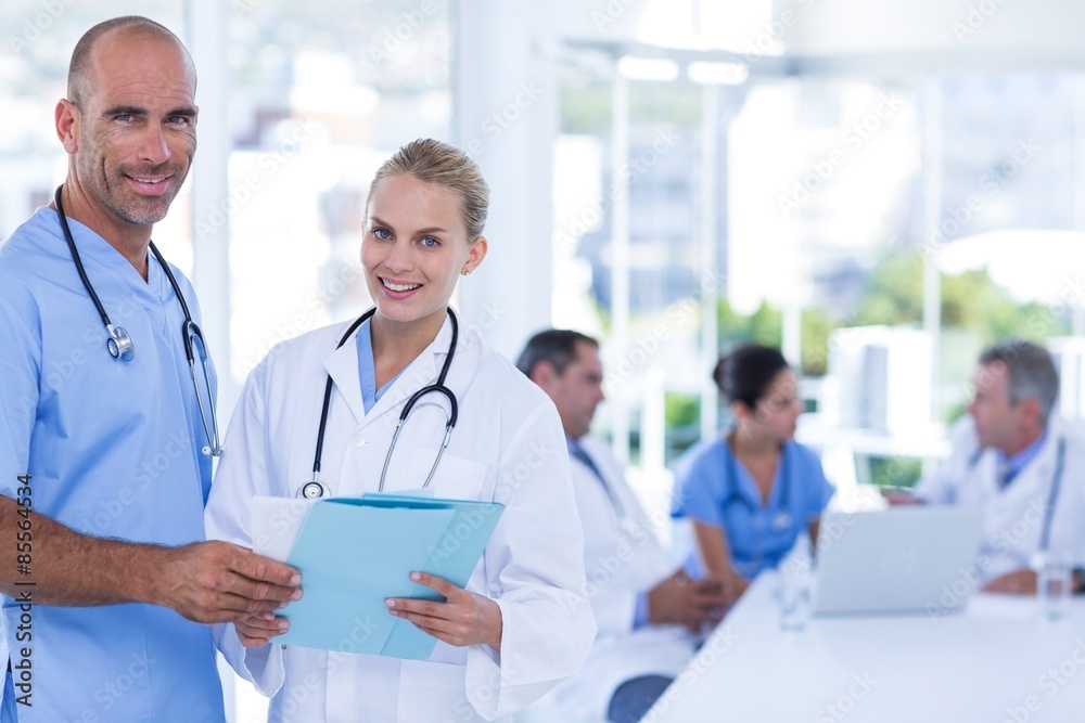 Two doctors holding clipboard while their colleagues working Two doctors holding clipboard while their colleagues working
