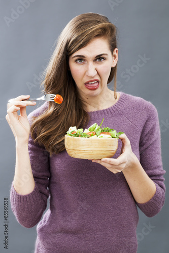 disgusted young girl being picky at eating mixed green salad with cherry tomatoes as vegetarian diet