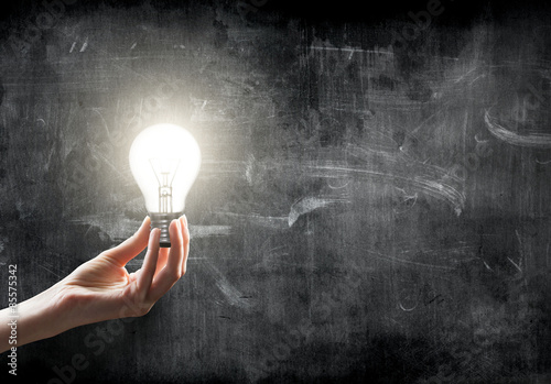 businesswoman holding Light bulb lamp on blackboard background with copy space