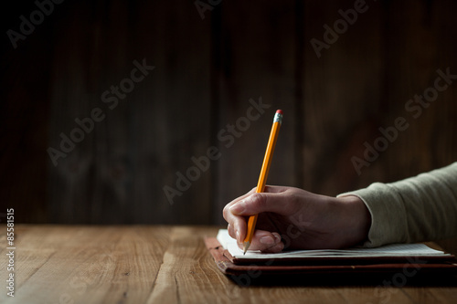 Closeup of woman's hand writing on paper over wooden table photo