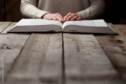 woman hands on bible. she is reading and praying over bible in a dark space over wooden table photo
